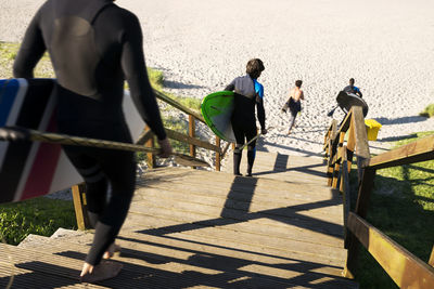 Rear view of people with surfboards moving down on steps at beach
