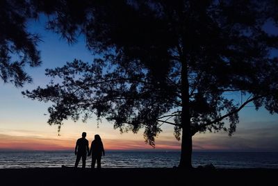 Silhouette people on beach against sky during sunset