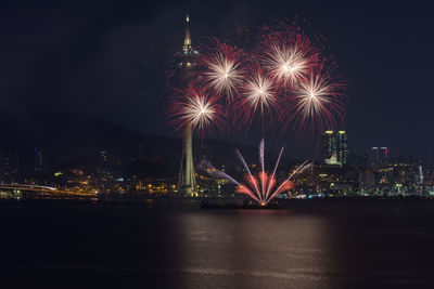 Firework display over illuminated city against sky at night