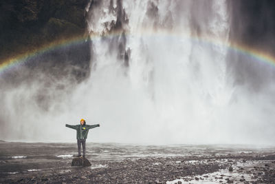 Rear view of man splashing water against waterfall