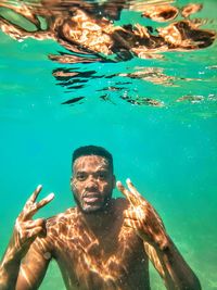 Portrait of shirtless man gesturing while swimming in sea