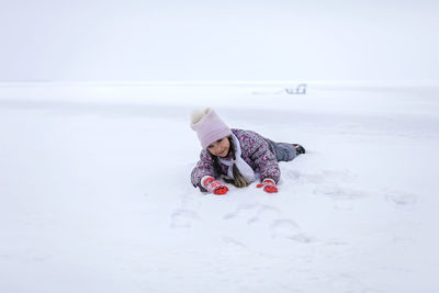 Portrait of cute girl lying down on snow during winter