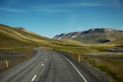 Empty road by green mountain against sky in iceland