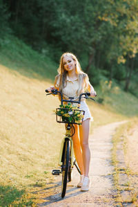 A happy girl in white shorts and a beige shirt with yellow flowers in a bicycle basket.