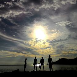Silhouette people standing on beach against sky during sunset