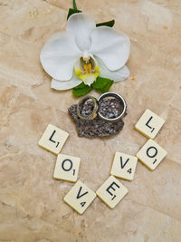 High angle view of wedding rings by flower and alphabets on toy blocks