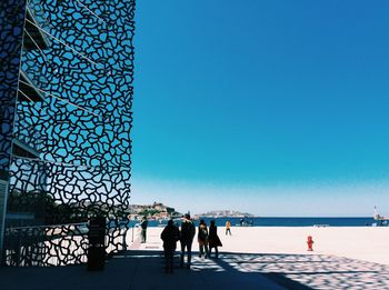 People by sea against clear blue sky