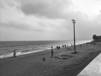 People at beach against cloudy sky