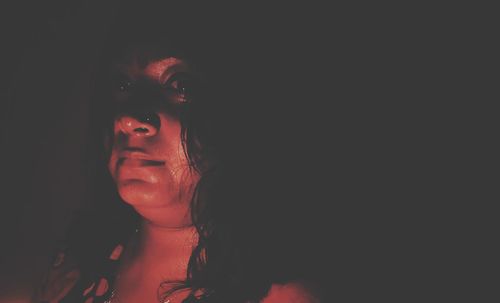 Portrait of young woman looking away against black background