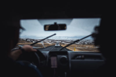 Two men driving a car on a in the rain on a paved road in iceland