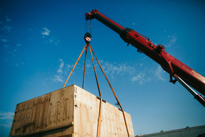 Low angle view of crane carrying box against blue sky