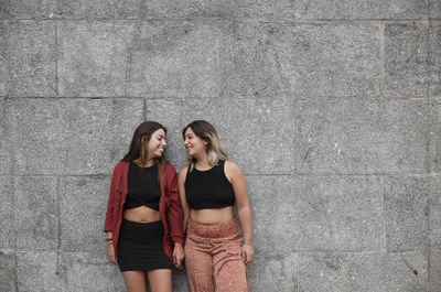 Two young girls standing against stone wall