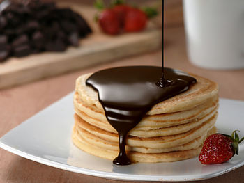 Close-up of melted chocolate pouring on stacked pancakes at table