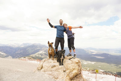 Portrait of couple with dogs standing on mountain against cloudy sky