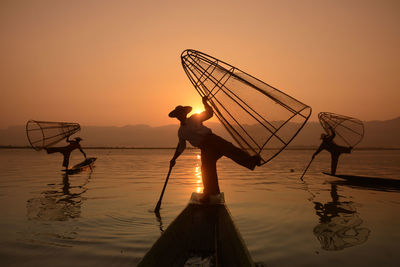 Silhouette men fishing in lake during sunset