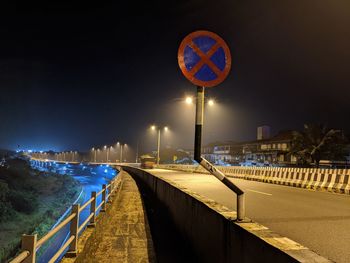 Illuminated street light by road against sky at night