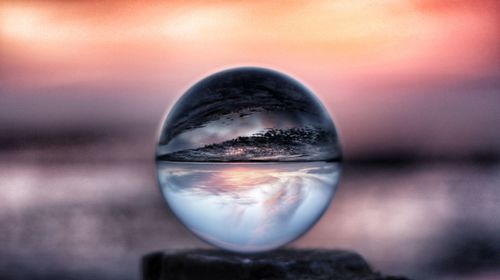 Close-up of water drops on crystal ball against sky during sunset