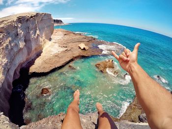 Low section of man gesturing shaka sign on cliff against sea