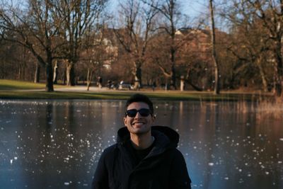 Portrait of smiling young man wearing sunglasses standing against lake