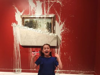 Portrait of smiling girl standing against red wall