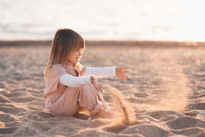 Side view of girl playing with sand at beach