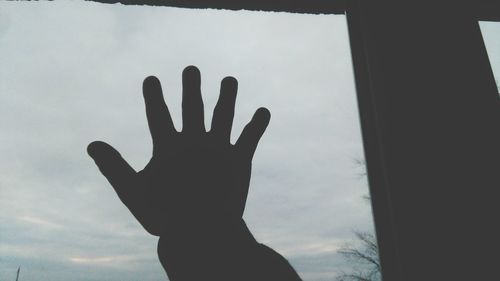 Silhouette of man hand against cloudy sky