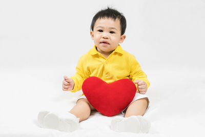 Portrait of cute girl holding heart shape against white background