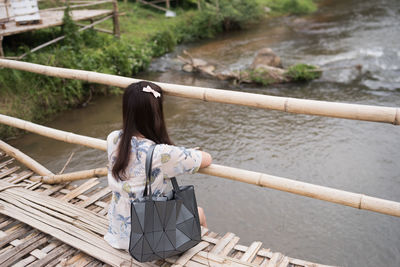 Woman sitting on footbridge over lake
