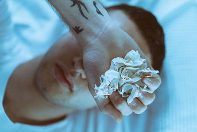 Close-up of man holding crumpled paper while lying down on bed