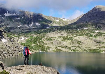 Rear view of hiker standing by lake against mountains