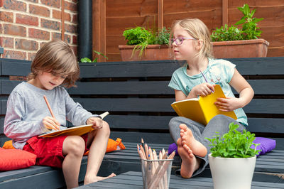 Two little friends from school sitting together in garden and doing homework.