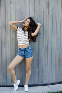 Full length portrait of young woman standing against wall