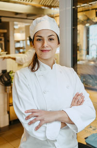 Happy female chef with arms crossed standing at door in commercial kitchen