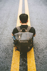 High angle view of man sitting with backpack on road