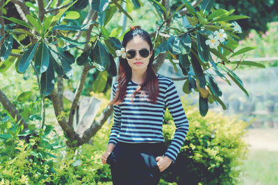 Portrait of woman wearing sunglasses while standing against tree