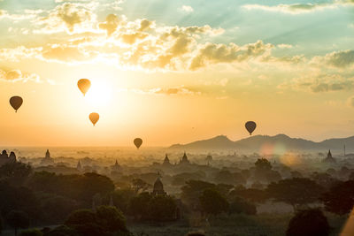 Hot air balloons flying over landscape against sky during sunset