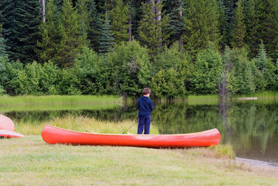 Red canoe moored by boy fishing at lake