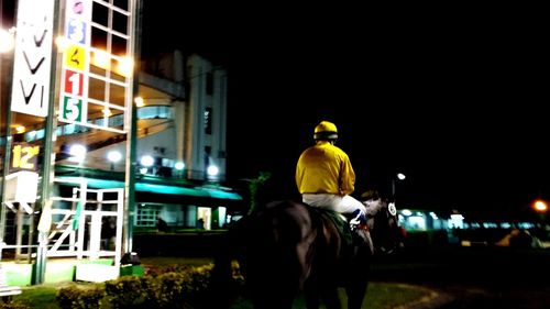 Rear view of man standing in illuminated city at night