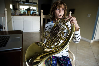 Girl playing french horn while sitting on chair at home