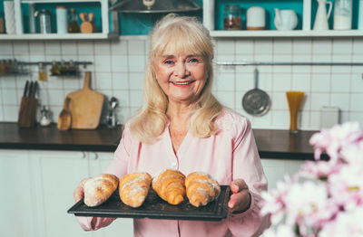 Portrait of smiling senior woman holding croissant