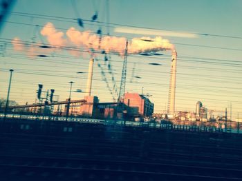 Illuminated railroad tracks by buildings against sky at dusk