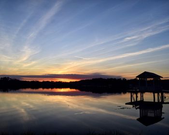 Silhouette building by lake against sky during sunset