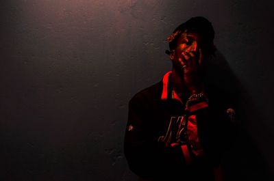 Man with hand on mouth standing against wall in dark