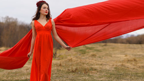 Portrait of young woman standing on field against sky