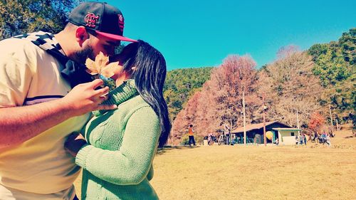Midsection of couple kissing in park against sky