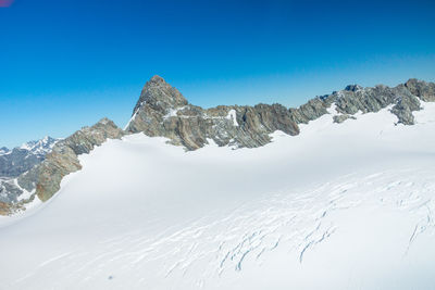 Low angle view of snowcapped mountains against clear blue sky