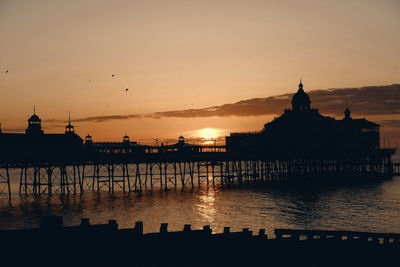 Silhouette building by sea against sky during sunset
