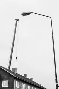Low angle view of crane by building against clear sky