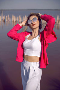 Portrait of young woman in pink and white clothes wearing sunglasses stand on pink lake 