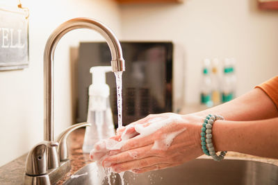 Midsection of woman with faucet in water at home